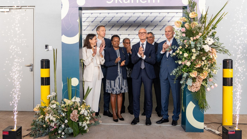 A group of executives and dignitaries applauding in front of a ceremonial arch, with fireworks and floral arrangements nearby.