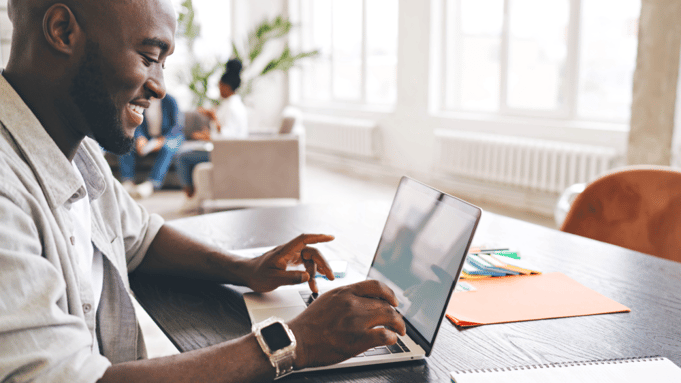 Smiling man sitting in front of a laptop, typing something